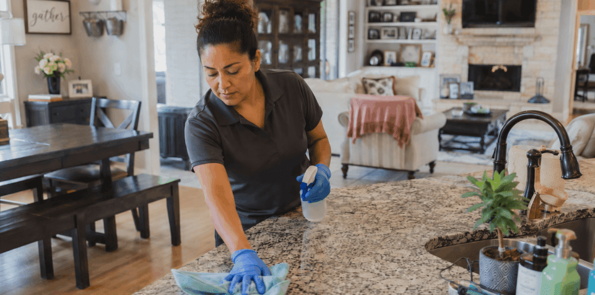 A cleaner wiping a kitchen island with a blue cloth.