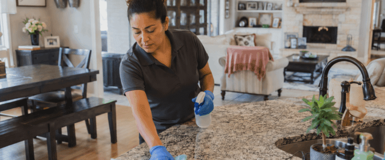 A cleaner wiping a kitchen island with a blue cloth.